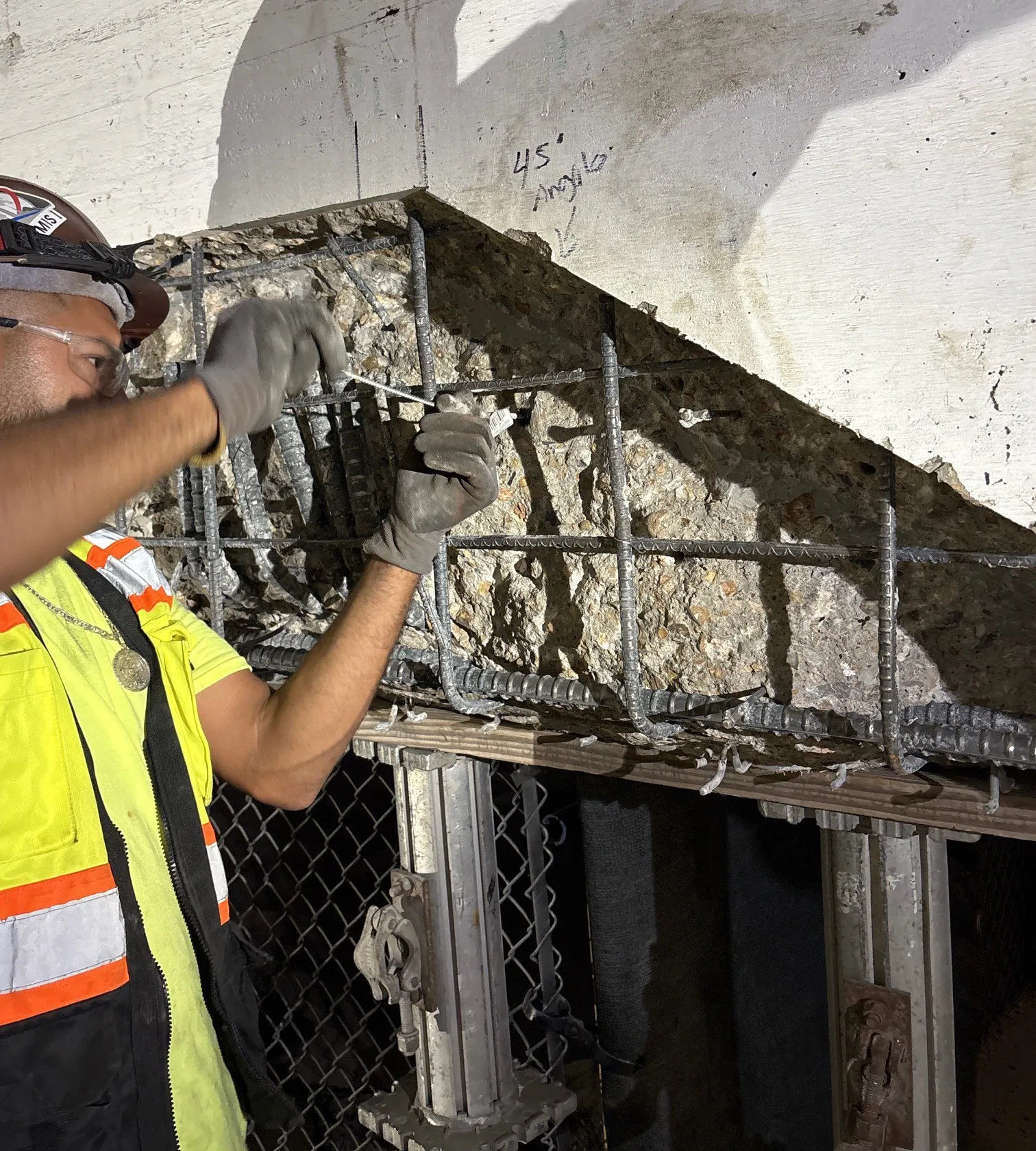 Worker inspecting exposed rebar and concrete during structural repair process.